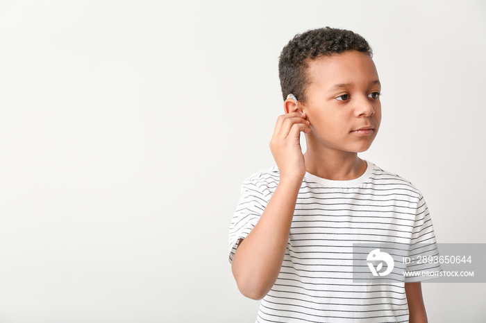 Little African-American boy with hearing aid on light background