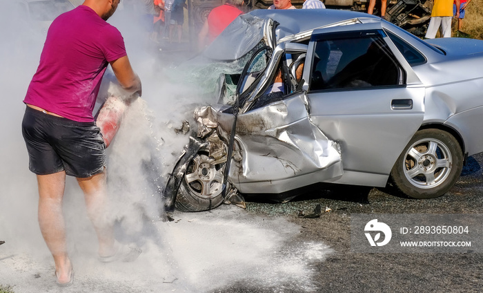 Man extinguishes the car with a fire extinguisher. Damaged vehicle closeup after car crash.