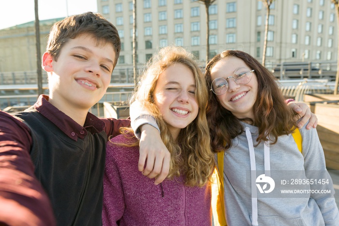 Portrait of three teen friends boy and two girls smiling and taking a selfie outdoors.