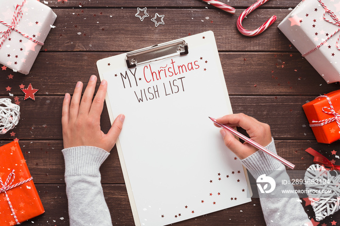 Girl writing her Christmas wish list on wooden background