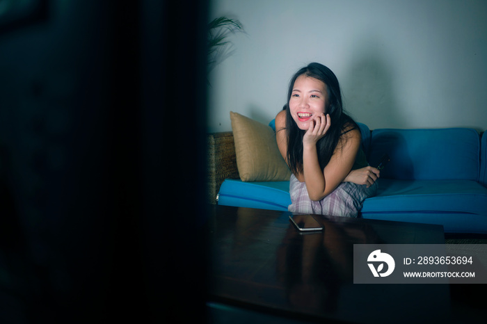 young happy and beautiful Asian Korean woman watching TV  at living room sofa couch enjoying funny t
