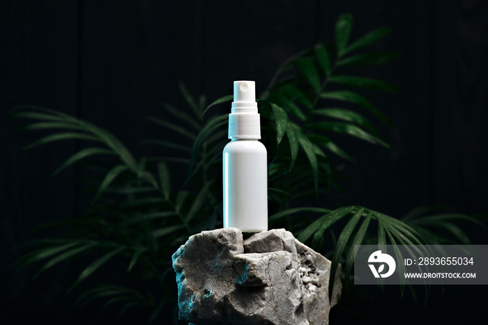 White plastic bottle spray on a white stone on a background of plants. Spray advertising photo. Mock