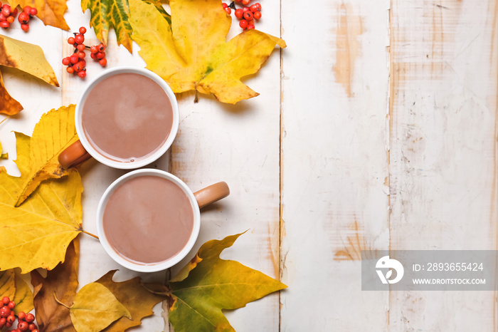 Cup of hot cacao drink with autumn leaves on white wooden background