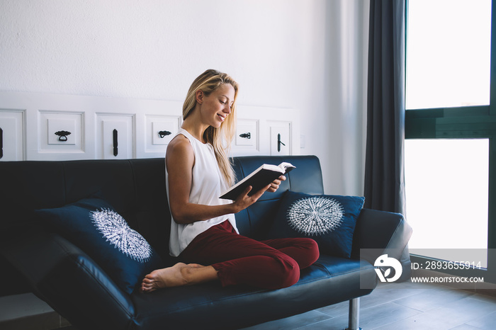 Beautiful woman dressed in casual look resting at comfortable couch and reading interesting bestsell