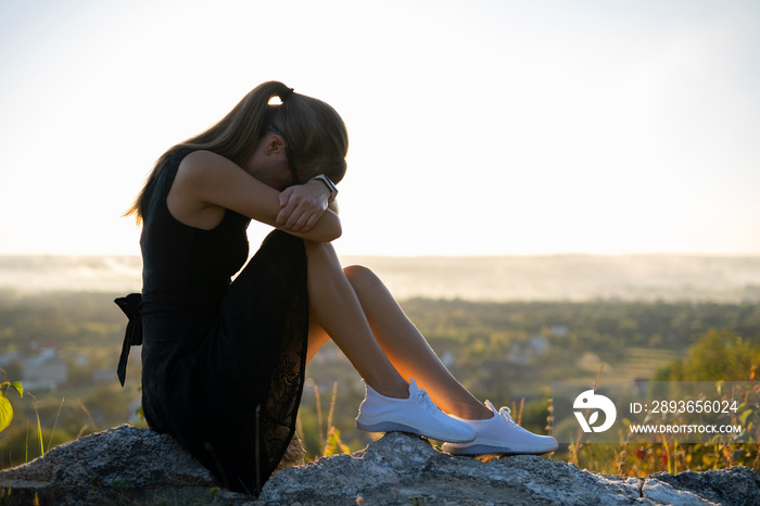 穿着黑色夏装的年轻沮丧的女人坐在山上，在户外思考苏