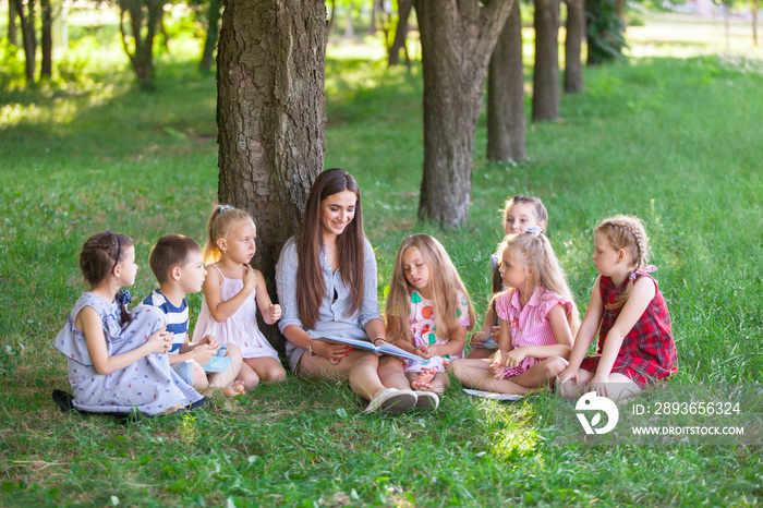 children hold a lesson with the teacher in the park on a green lawn.