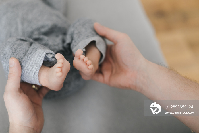 Young mother or doctor hands holding little feet barefoot of newborn on gray background. Happy momen