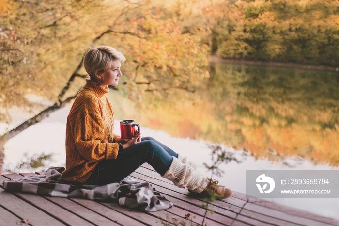 坐在湖边喝热茶的女人。秋天很舒服。