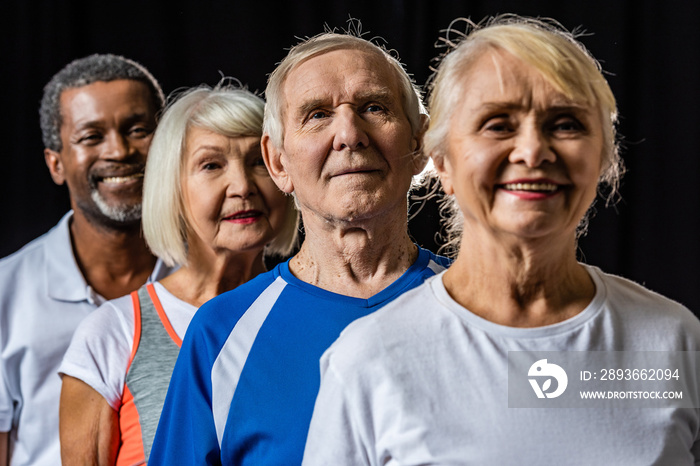 smiling multicultural senior sportspeople standing isolated on black