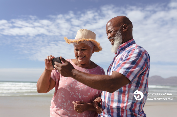 Happy senior african american couple using smartphone at the beach