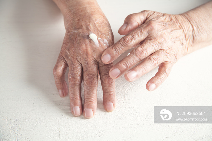 Elderly woman applies the cream on the hand.