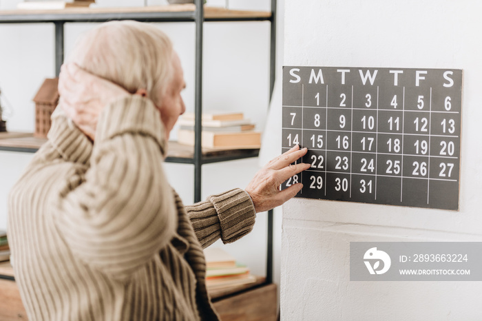 man with grey hair touching wall calendar and head