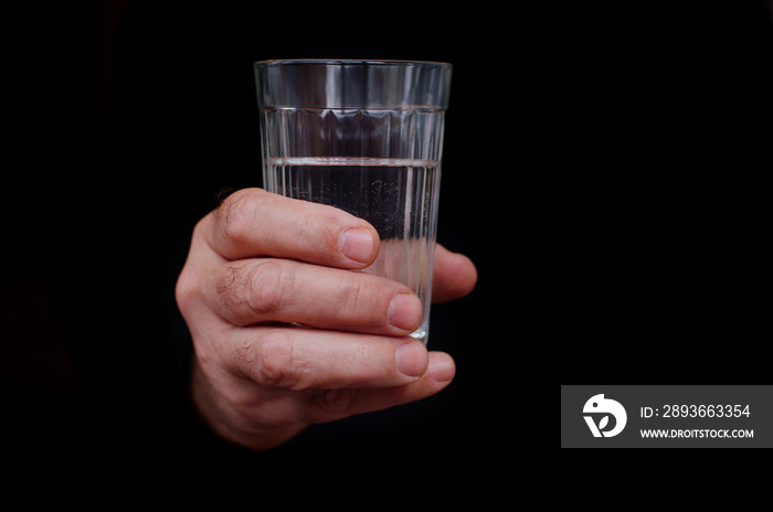 Male hand holding a glass of water on black background