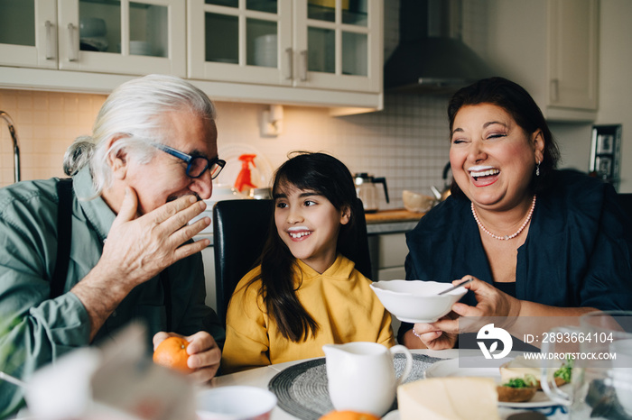 Elderly man talking to grandchild and woman with milk mustache during breakfast at home