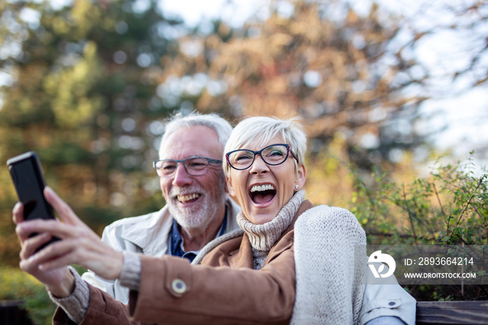 MAture couple taking selfie by mobile phone while sitting on bench in public park