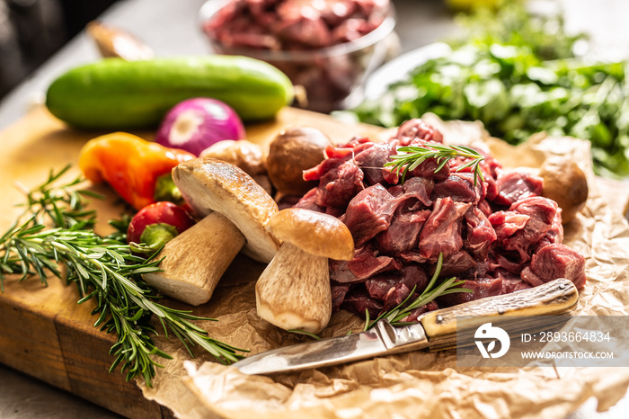 Sliced deer meat prepared for stew of game forest mushrooms herbs vegetables and knife