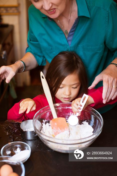 Grandmother with granddaughter (4-5) preparing cake in kitchen