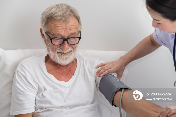 Happy nurse checking and measuring elderly man blood pressure in bedroom at nursing home