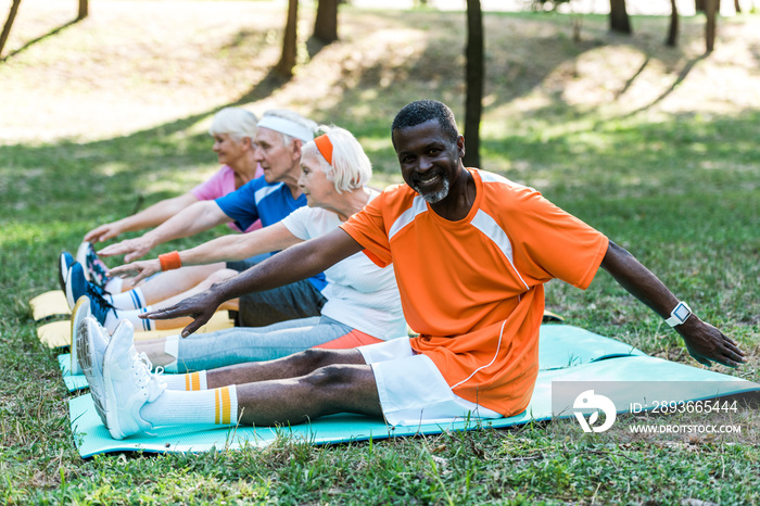 selective focus of multicultural retired men and woman in sportswear exercising on fitness mats