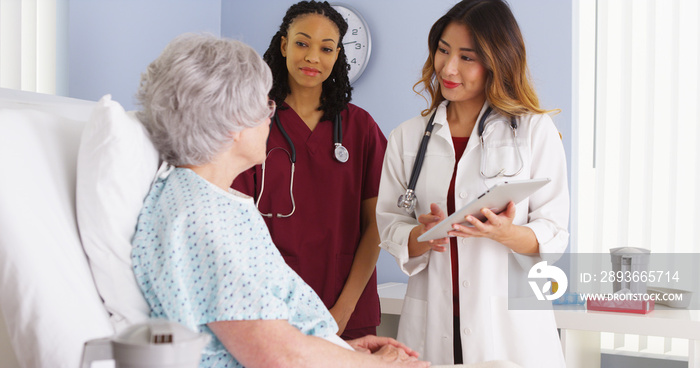 Japanese doctor and black nurse talking to elderly woman patient in hospital bed