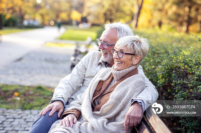 Mature couple sitting on bench in public park talk and smile