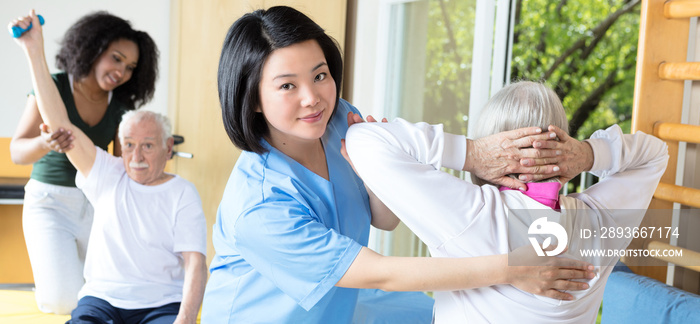 Rehab clinic gym. Elderly man and woman assisted by nurses