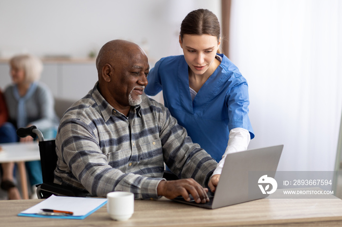 Young woman nurse helping black senior man using laptop