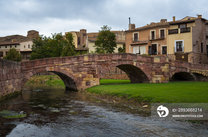 Scenic view of a medieval bridge made with reddish stone blocks and the castle on the top of the hil