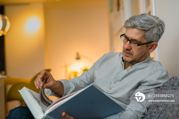 middle aged man reading book relaxed at his sofa