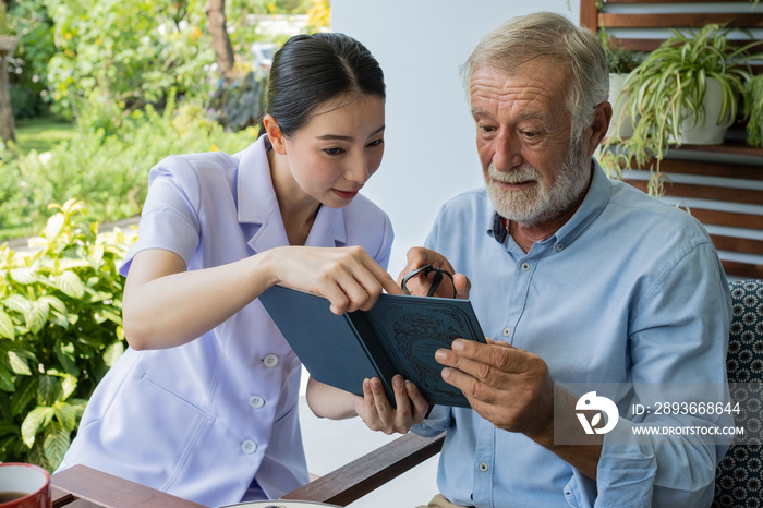 senior man happiness with smiling nurse, read book together at balcony near garden at nursing home