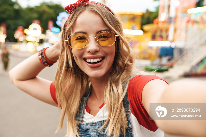 Cheerful happy young blonde woman in amusement park take selfie by camera.