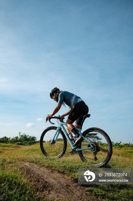 A young bearded cyclist is biking through a field