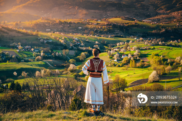 A young man in a Slovak folk costume looks at the spring landscape in the village of Hrinova in Slov