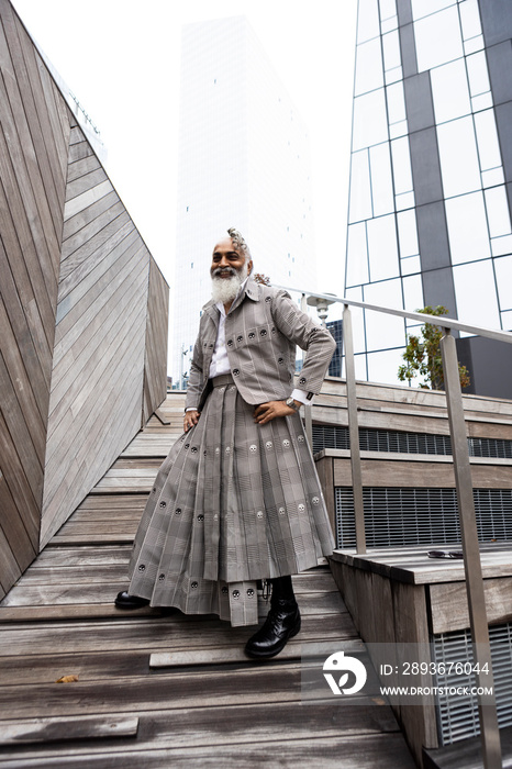 smiling man with gray hair and beard wearing skirt suit in modern city location