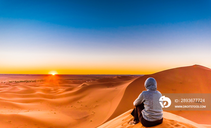 摩洛哥Mhamid旁边的撒哈拉沙漠中，一名妇女在享受日出
