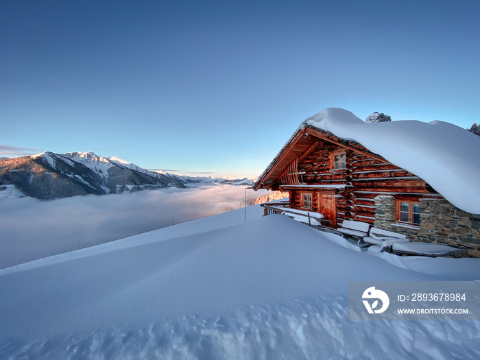 日出时，在蓝天的映衬下，奥地利阿尔卑斯山上的一座被雪覆盖的小屋古老的农舍。