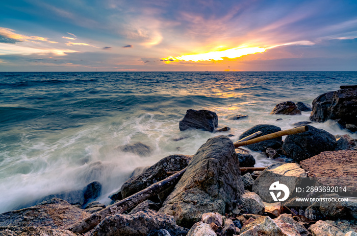 Ocean water splash on rock beach with beautiful sunset sky and clouds. Sea wave splashing on stone a