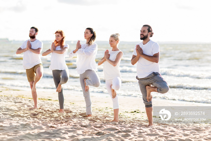 people making yoga in tree pose on summer beach