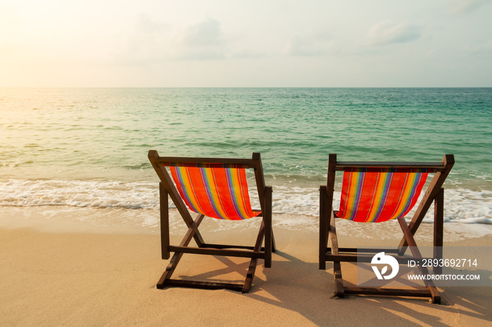 Two beach chairs on the sand beach with the light of the sun