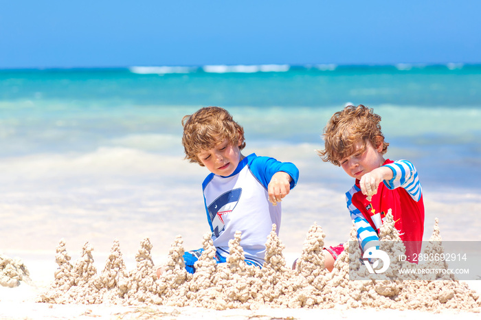 两个小男孩在岛上的热带海滩上建造一座沙城堡，玩得很开心。健康的chi