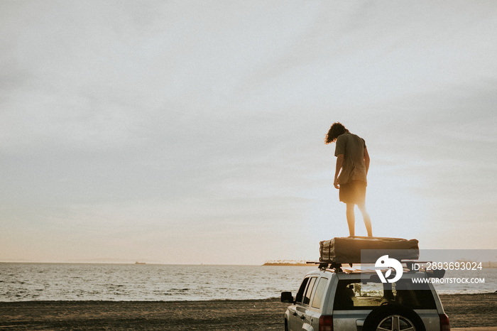 Man standing on a car top at the beach in California, USA