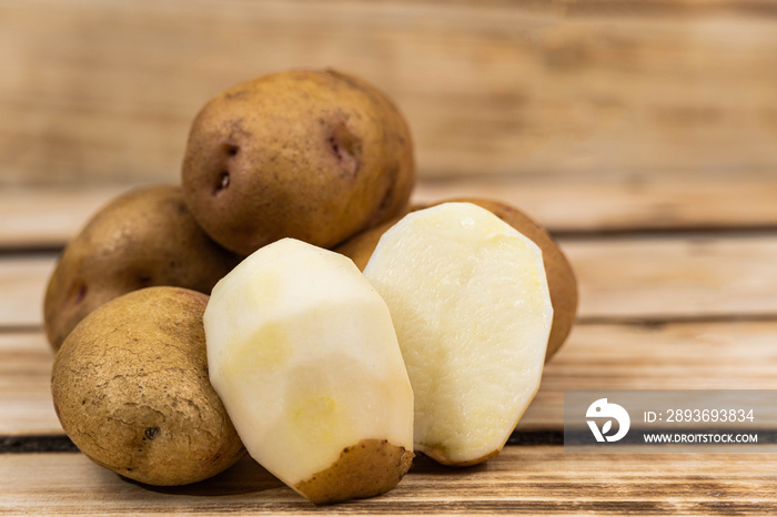 peeled potatoes in the foreground on a wooden background.