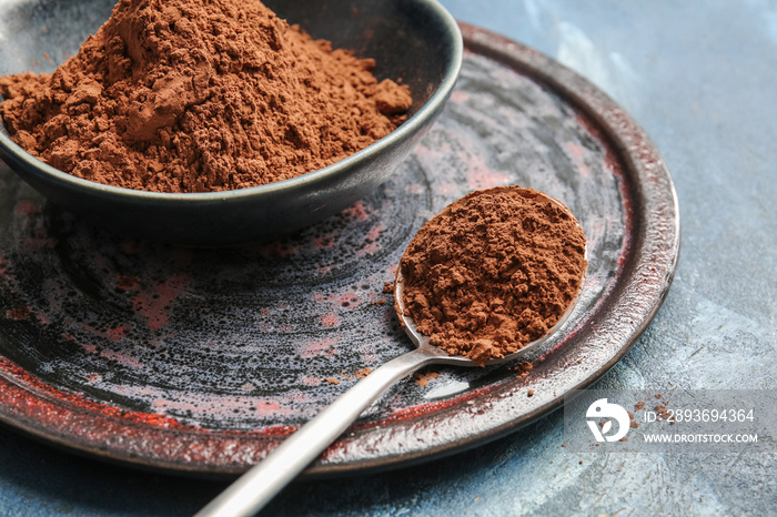 Bowl and spoon with cocoa powder on color background