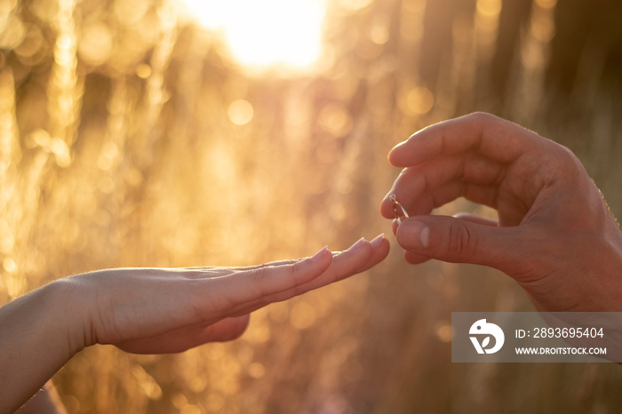 A man puts a wedding ring on a womans hand. Outdoors photo on sunset background. Will you marry me 