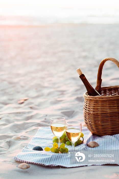 Two wine glasses, grapes, wicker basket on beach