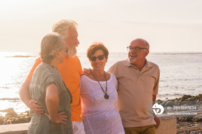 group of four senior and mature people with a friendship at the beach talking and enjoying together 