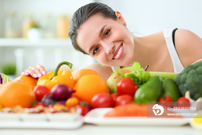 Young and cute woman sitting at the table full of fruits and vegetables in the wooden interior