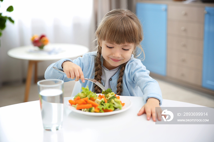 Small girl eating vegetables in kitchen