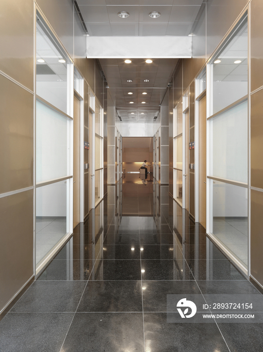 Tiled floor with glass paneled wall and recessed lights along narrow hallway in hotel