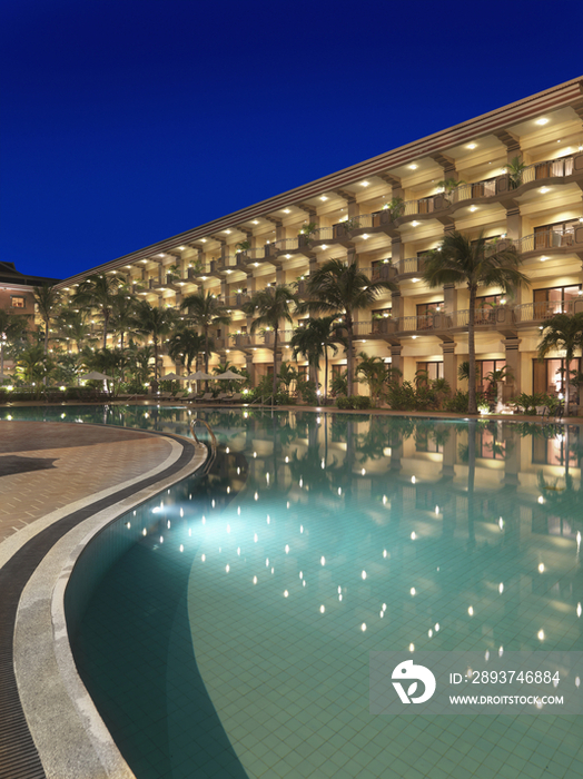 Illuminated hotel building with swimming pool at dusk